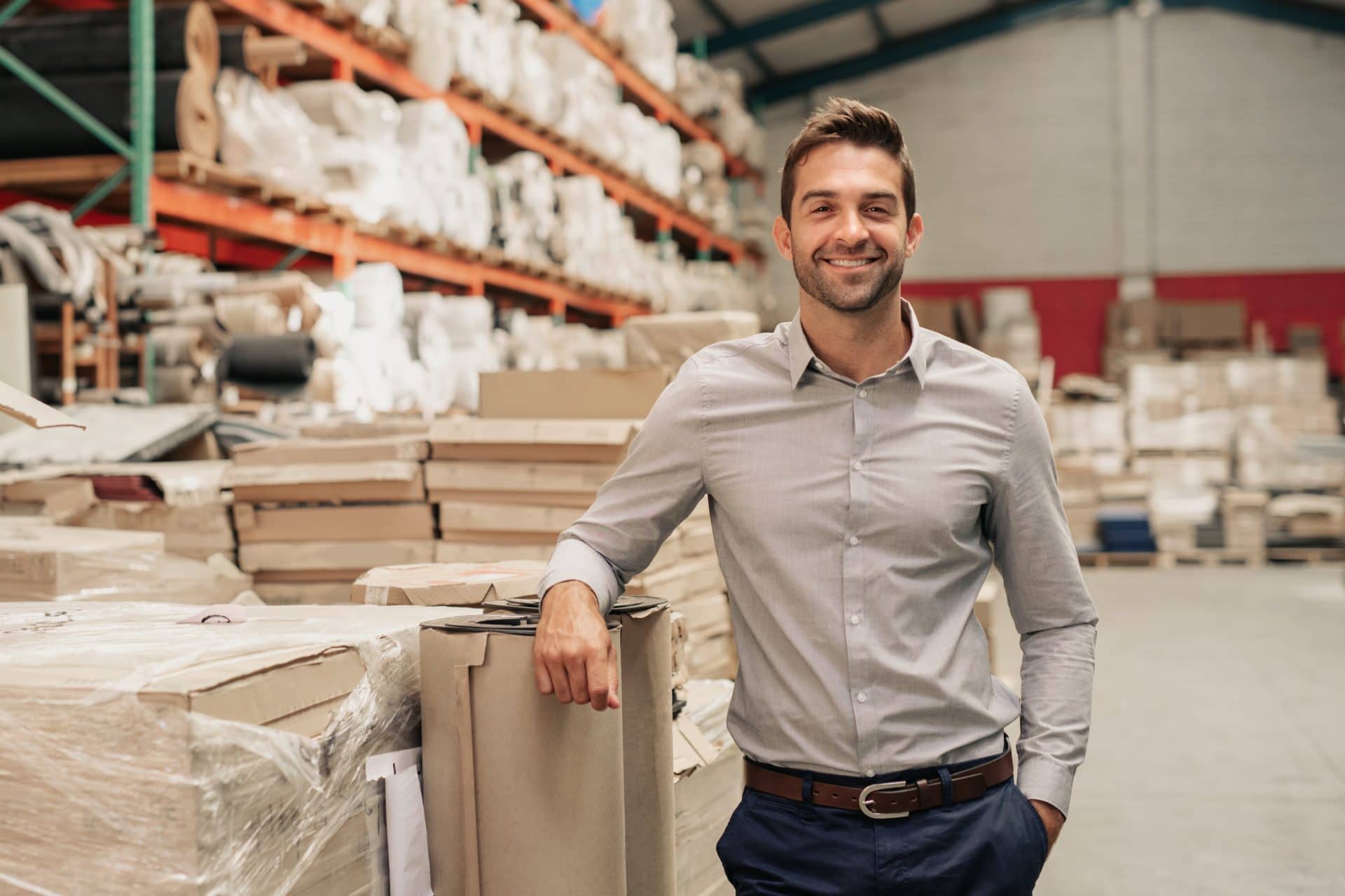 Manager smiling while leaning against stock in a large warehouse