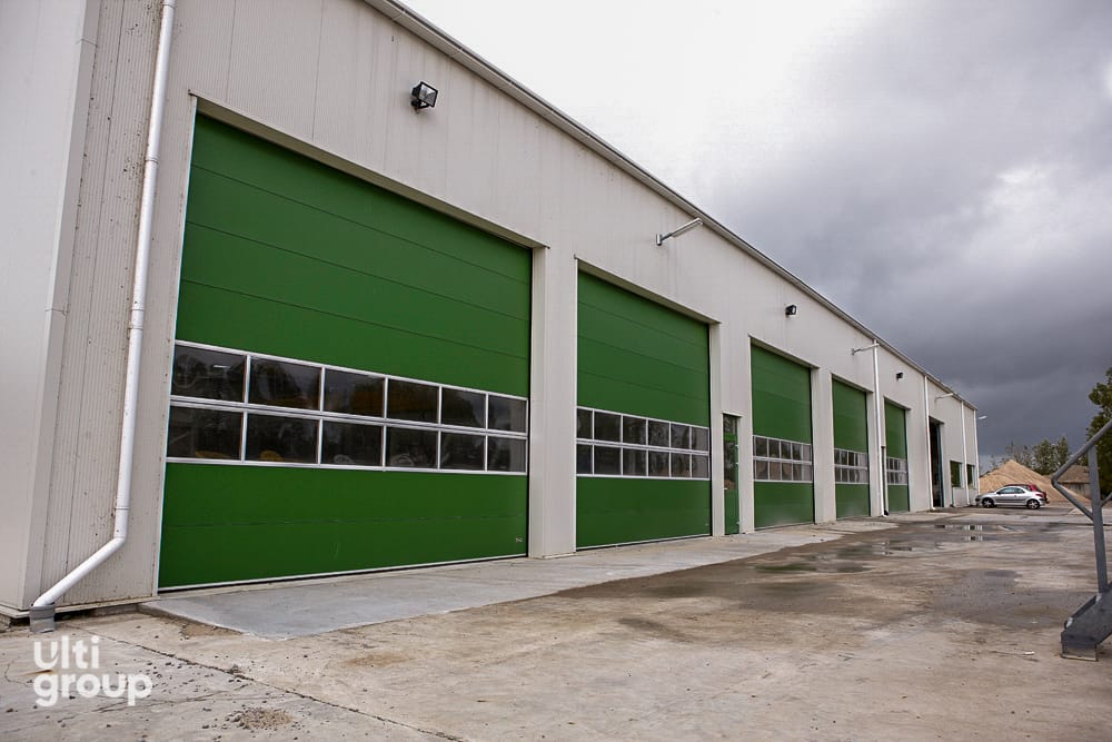 Green sectional overhead doors installed on a concrete industrial facility.