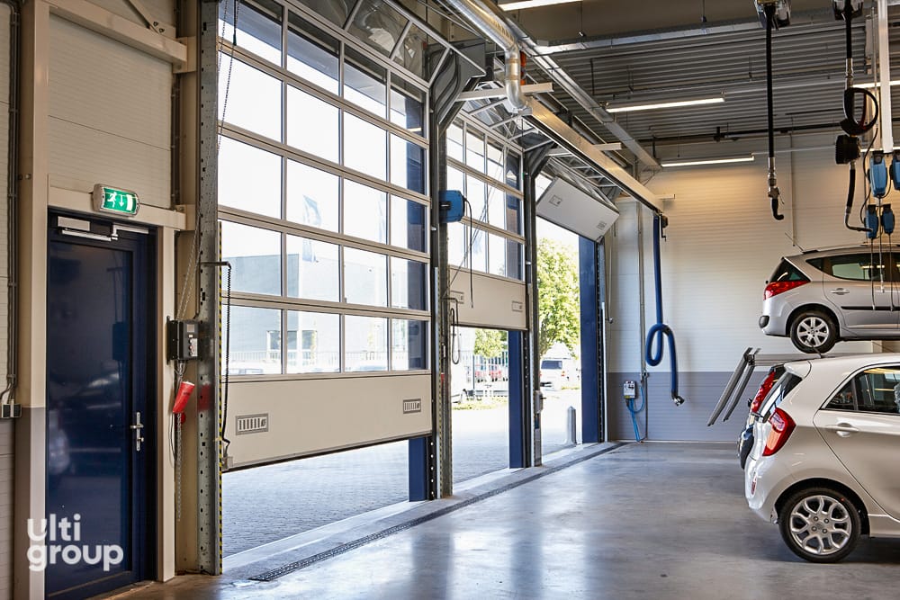 Stacking sectional doors partially open in a vehicle service workshop.