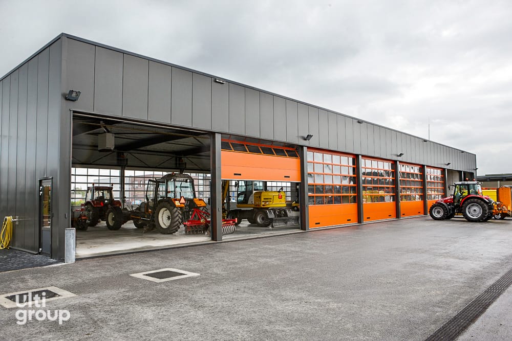Orange and glazed sectional stacking doors on a large grey industrial workshop.