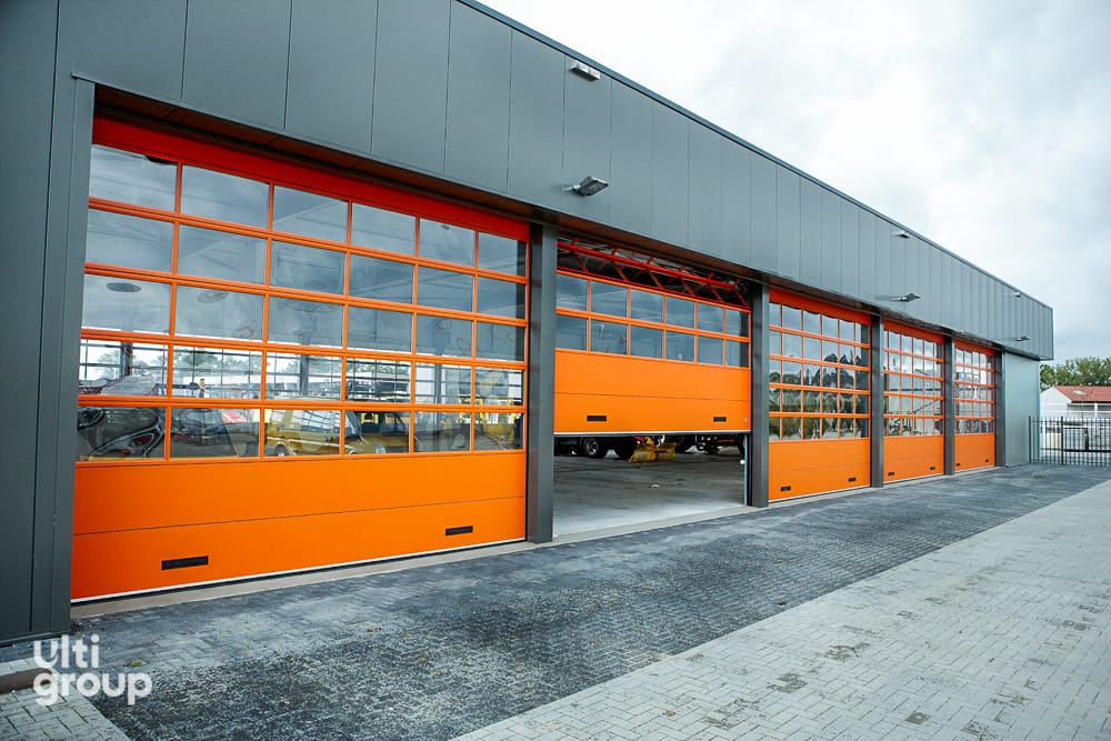 Orange and glass sectional industrial doors on a grey warehouse facade.
