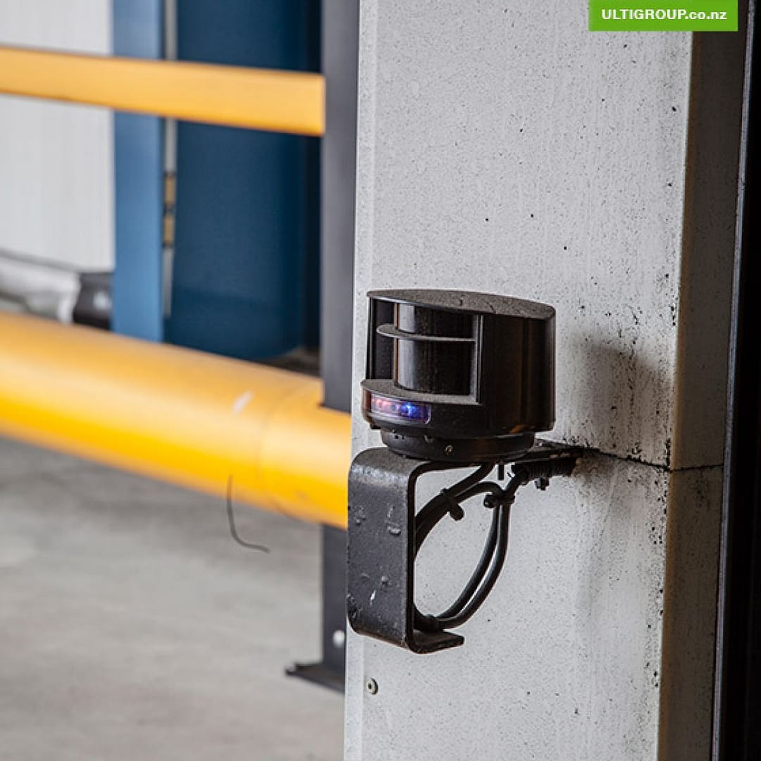 Black laser sensor mounted on a concrete wall for industrial door activation.