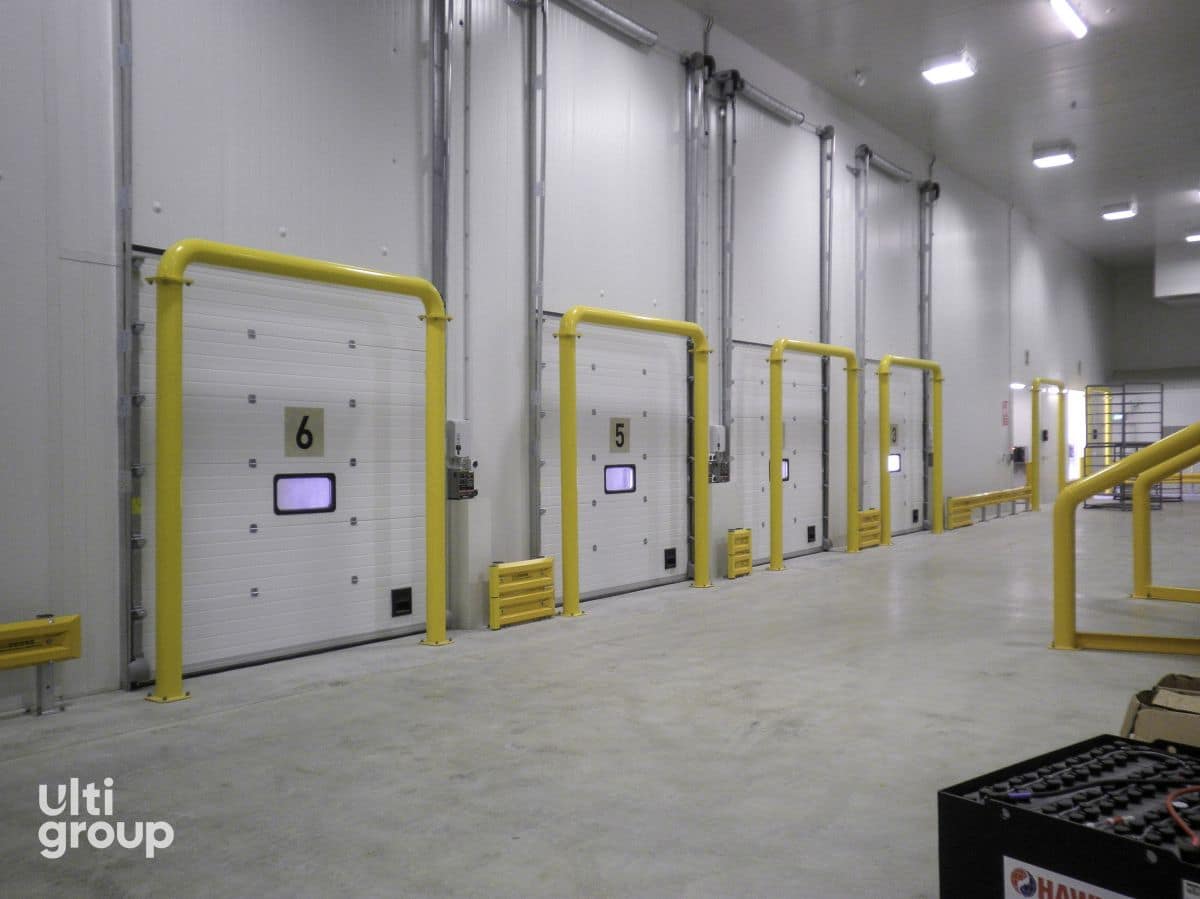 Insulated sectional doors with yellow full frame bollard protection in a warehouse.