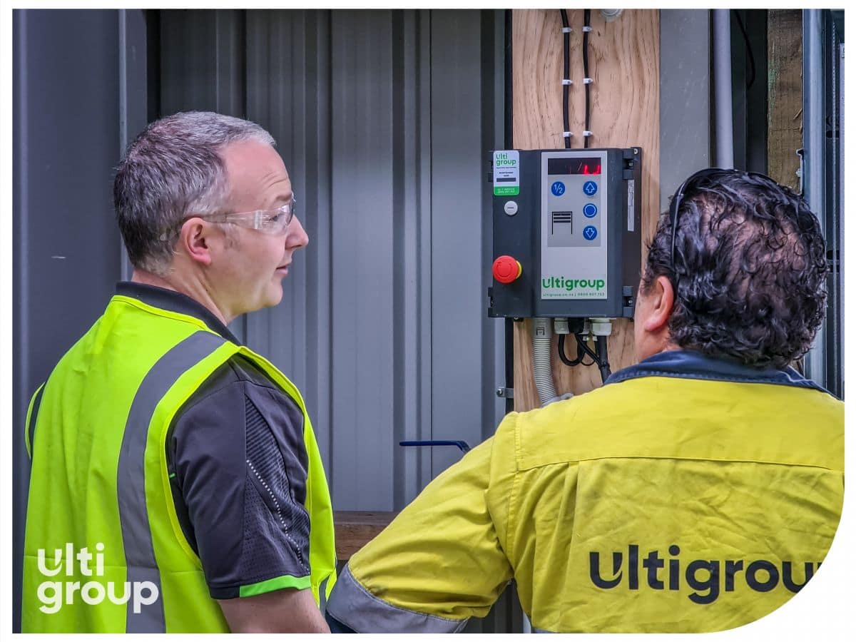 Two technicians inspecting an Ulti Group industrial door control panel.