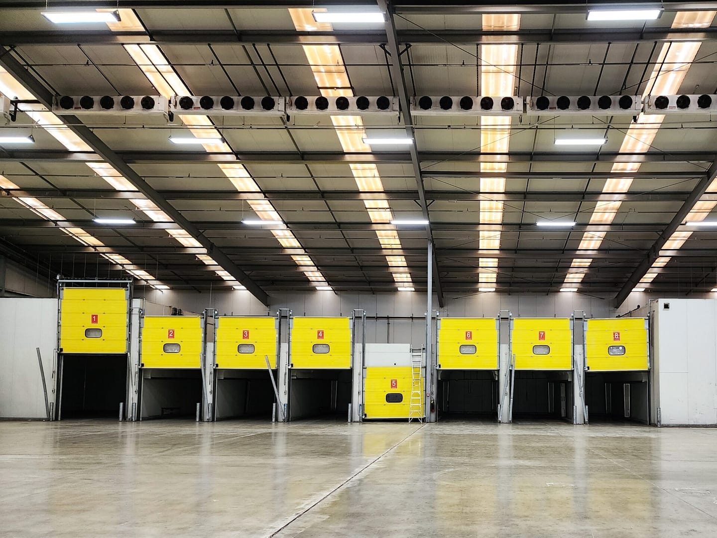 Row of yellow vertical storing dock levellers in a large warehouse facility.