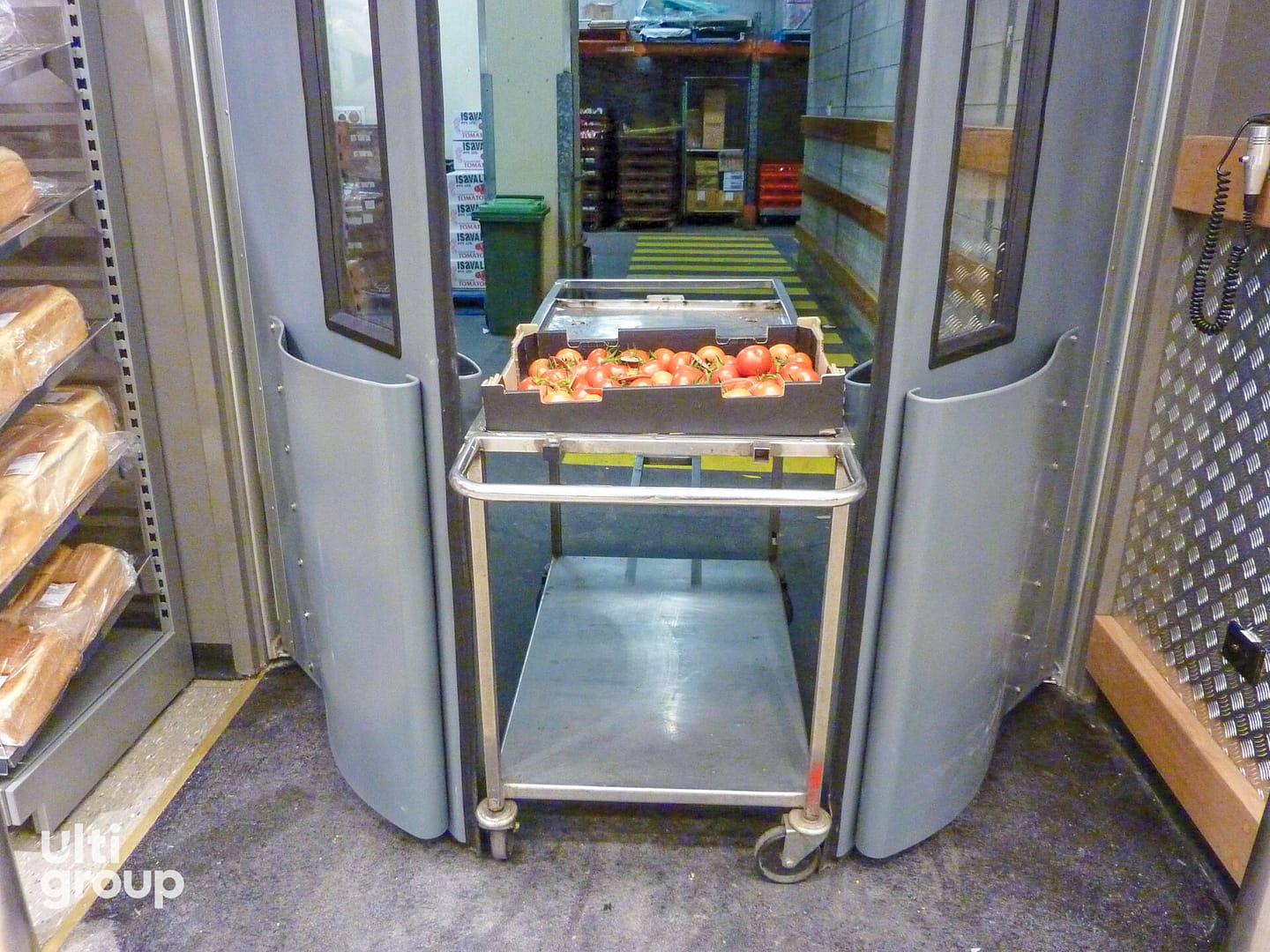Metal trolley passing through grey swing doors with protective bumpers.