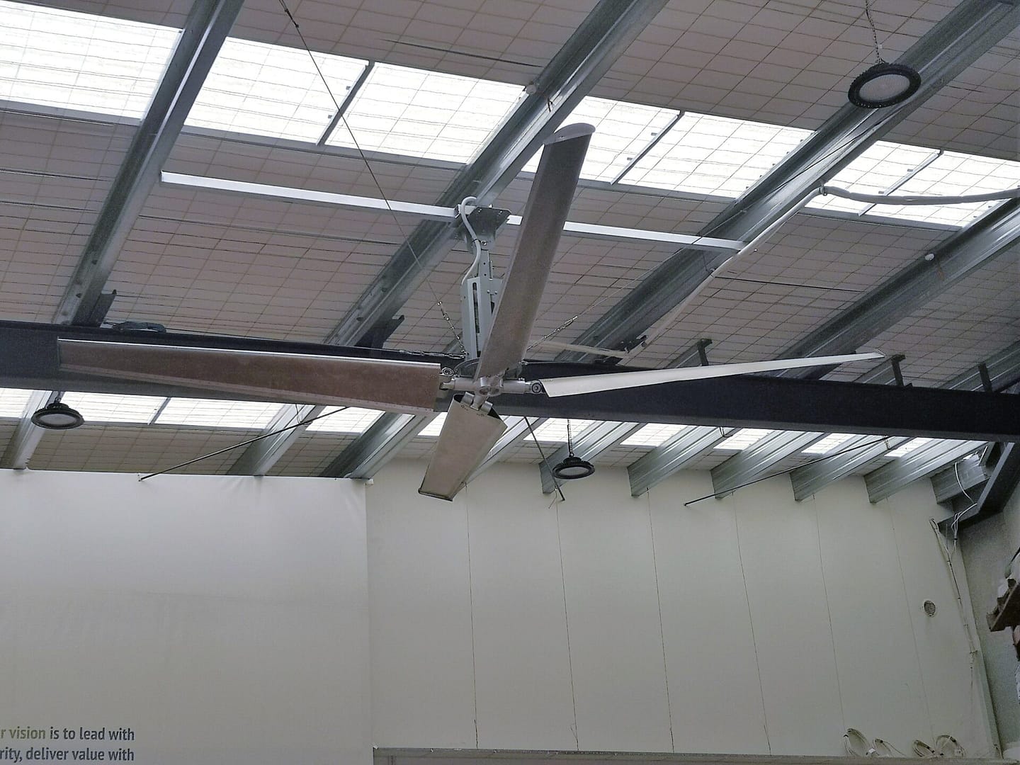 Large industrial ceiling fan installed in a warehouse with skylights.