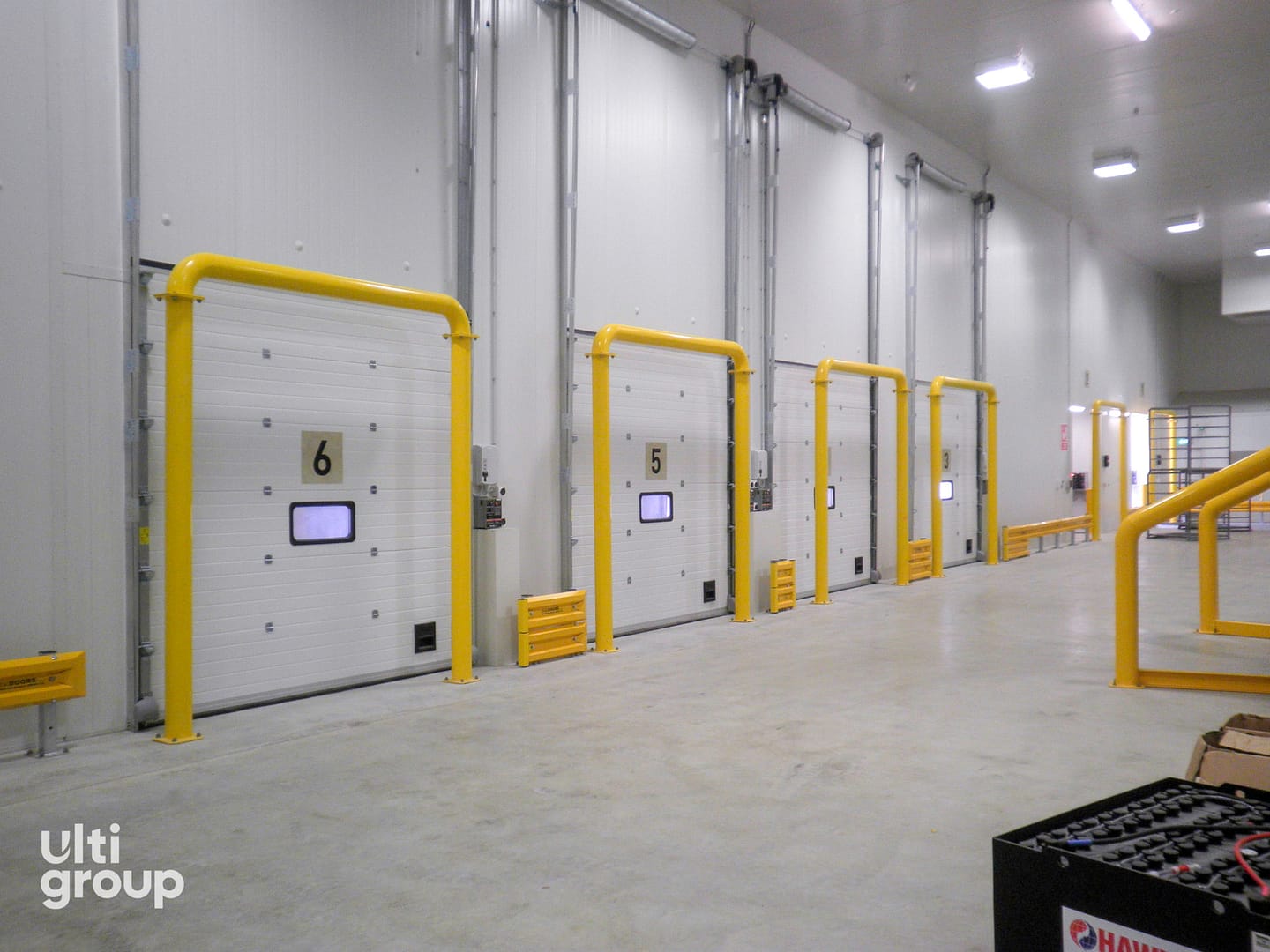 Insulated sectional doors with yellow full frame bollard protection in a warehouse.