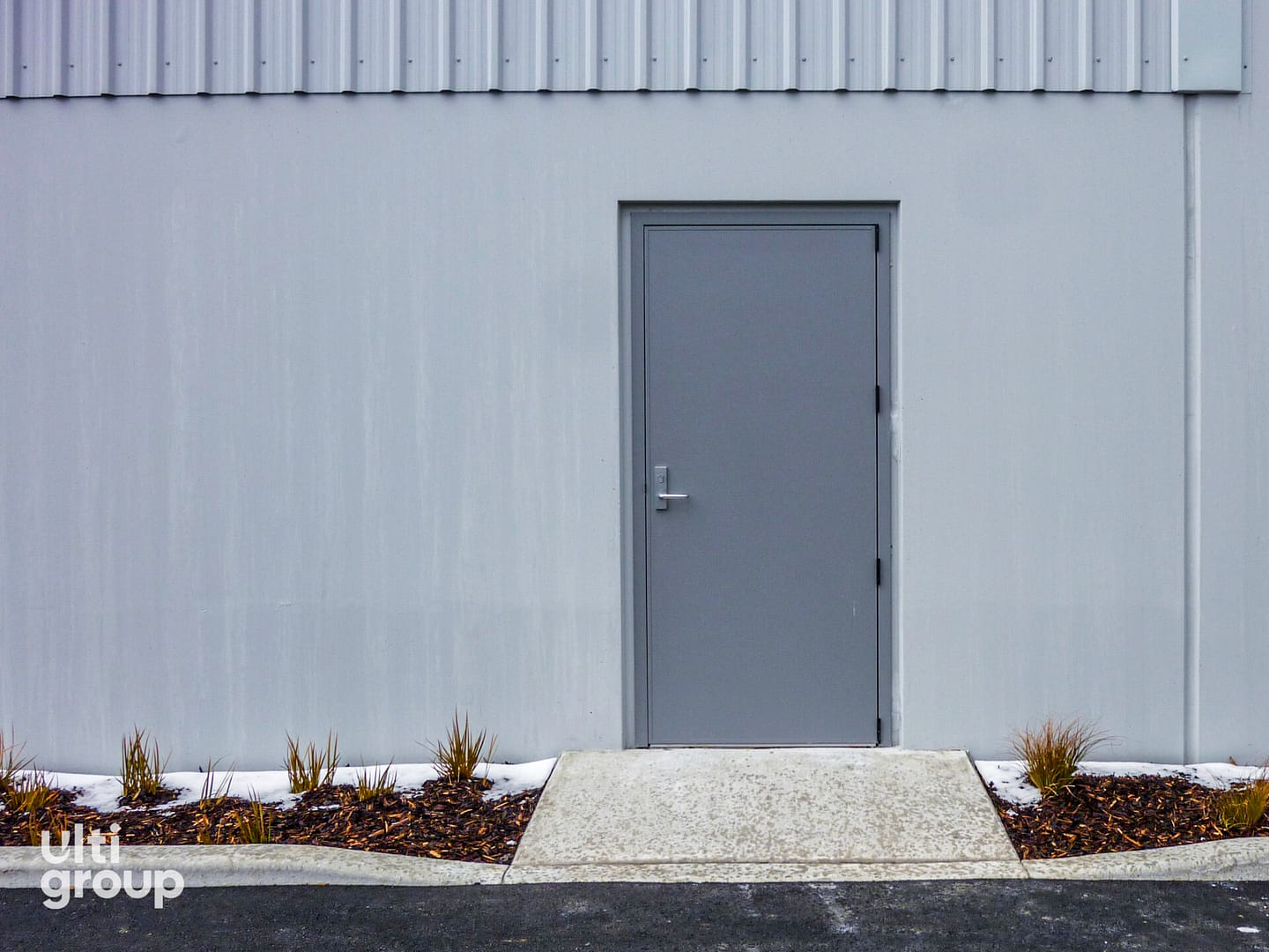 Grey steel personal access door installed in a concrete industrial wall.