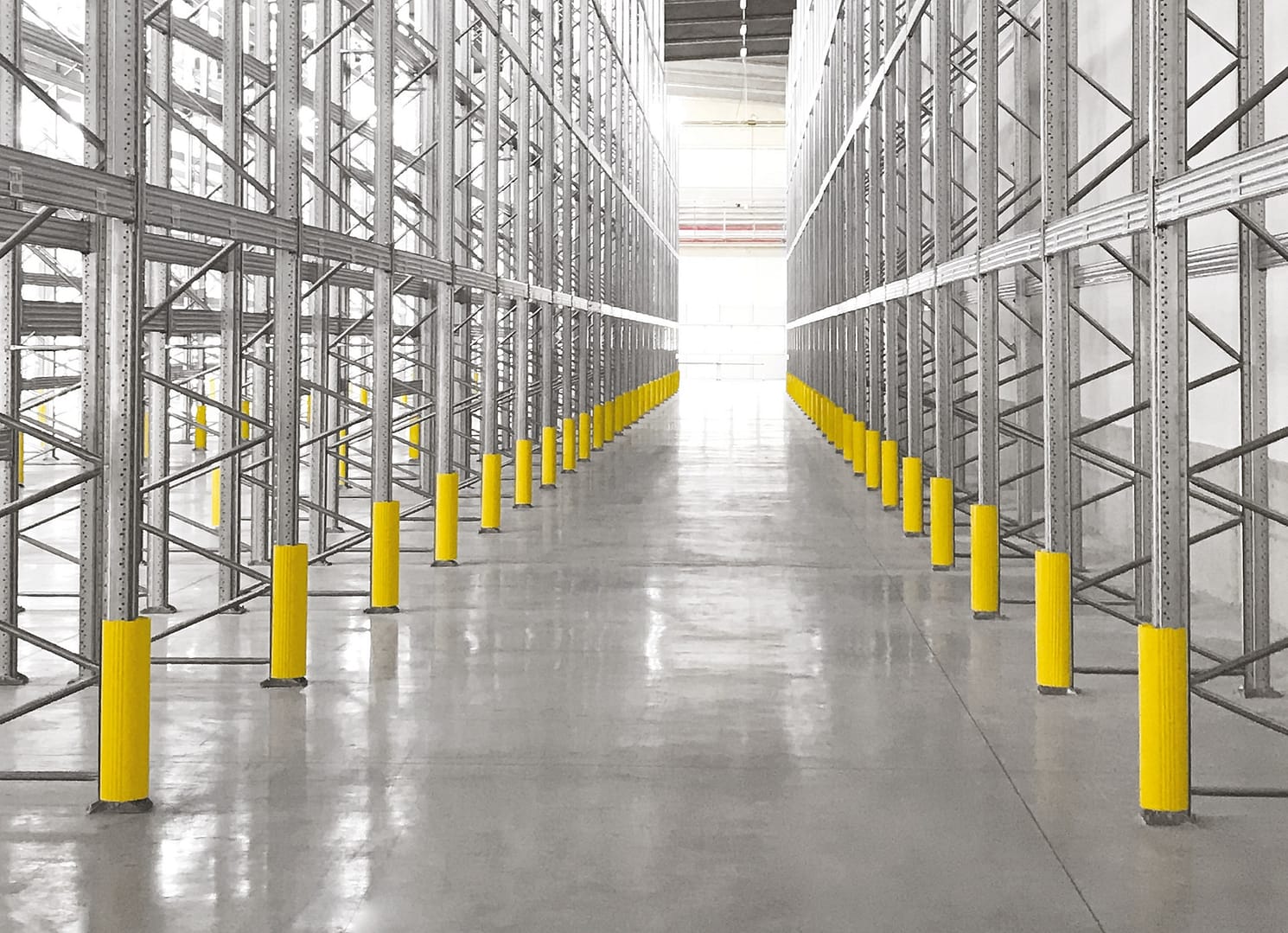 Yellow rack protectors installed on industrial shelving uprights in a warehouse.
