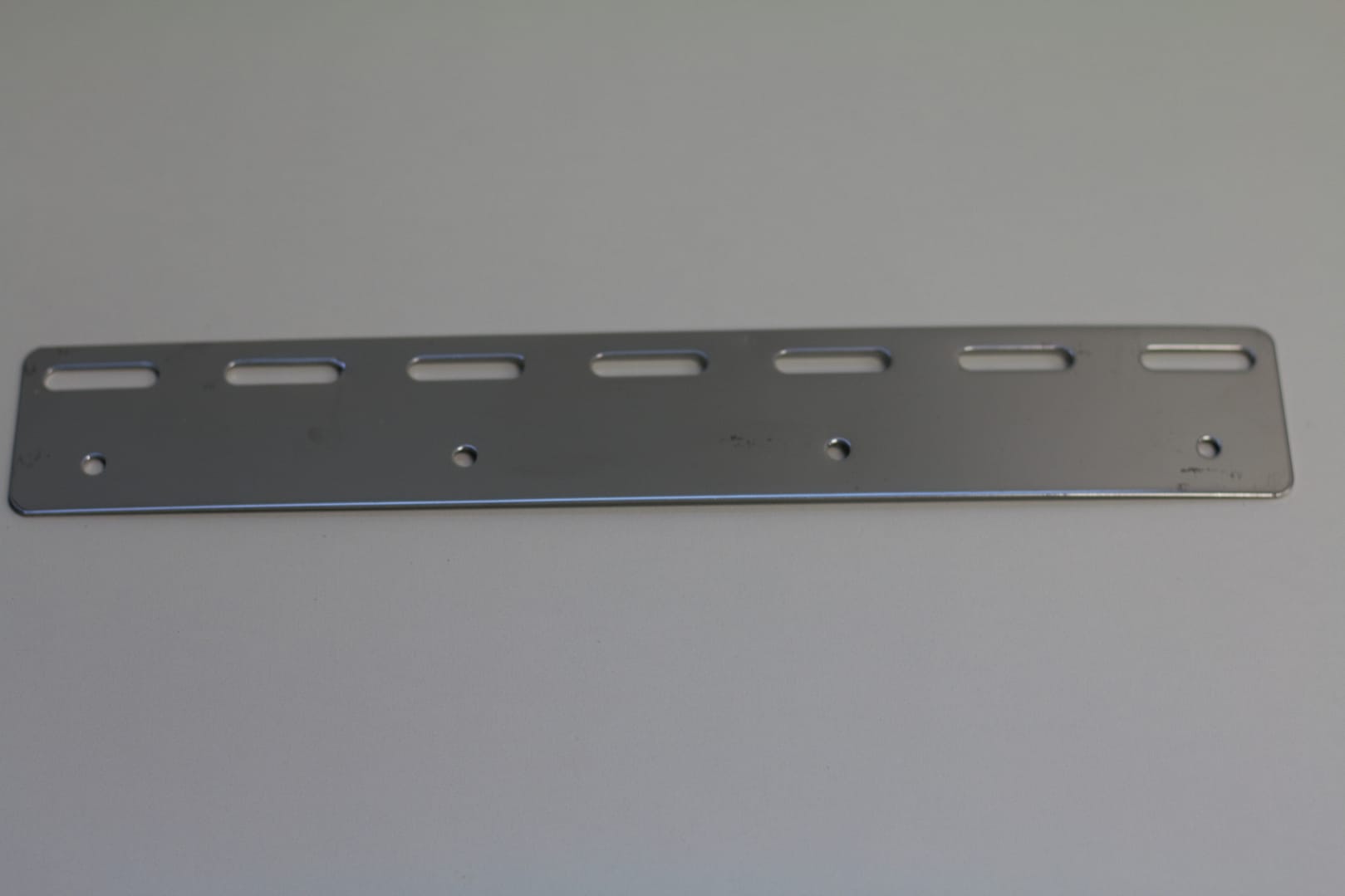 Stainless steel mounting bracket with slotted and circular holes.