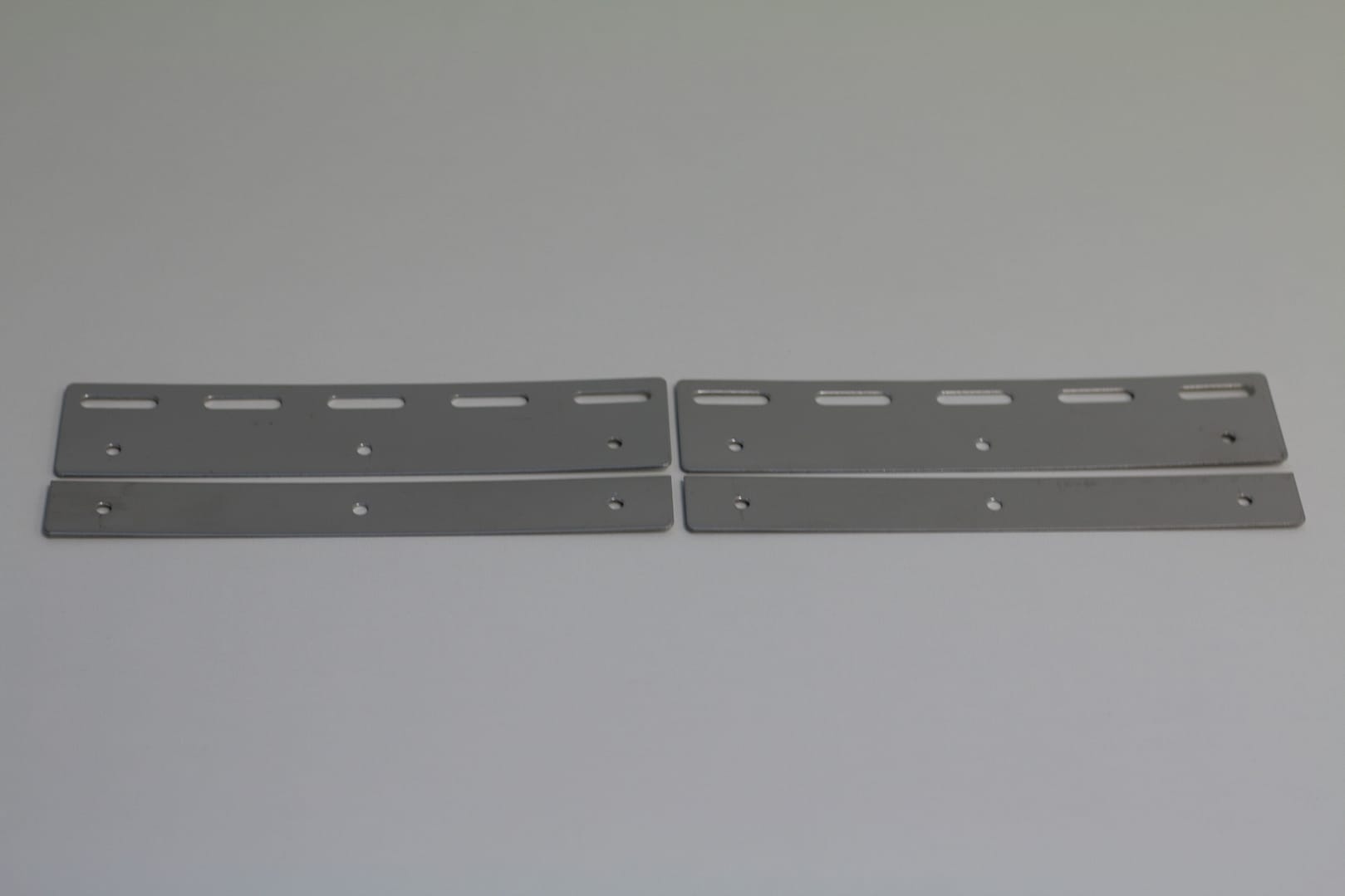 Four grey metal mounting plates with pre-drilled holes and slots.