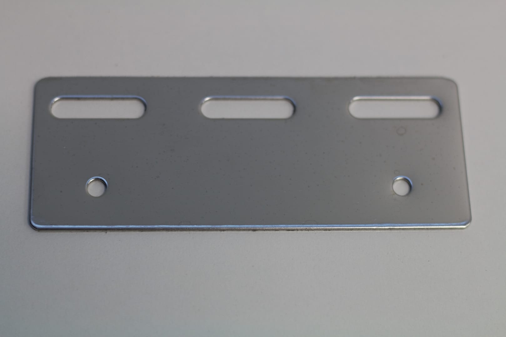 Rectangular stainless steel mounting plate with three slots and two holes.