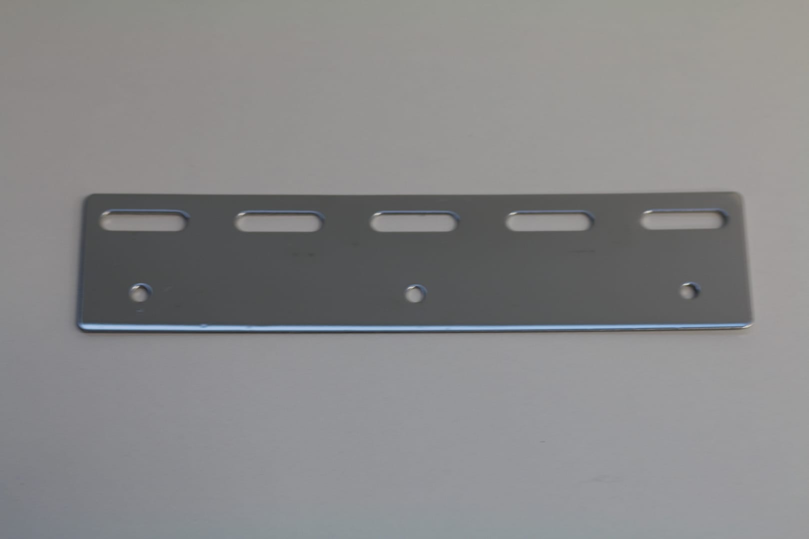 Stainless steel mounting plate with five horizontal slots and three circular holes.