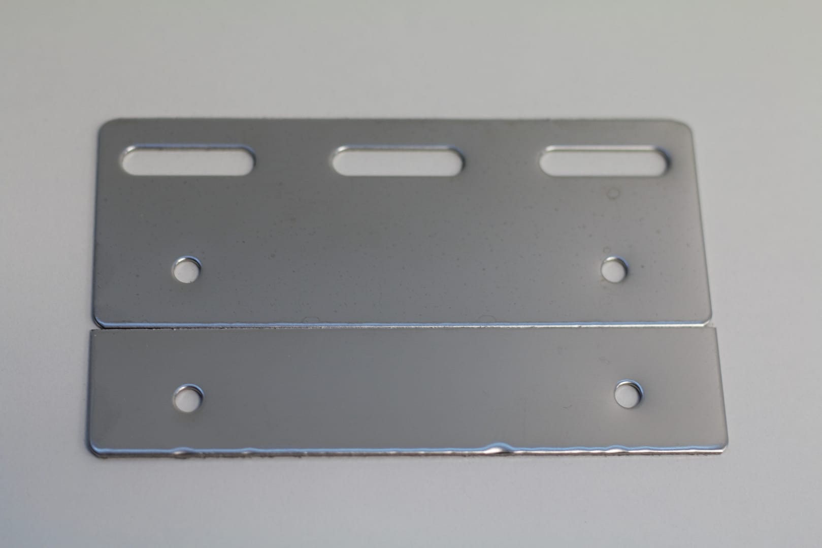 Two rectangular stainless steel mounting plates with pre-drilled holes and slots.