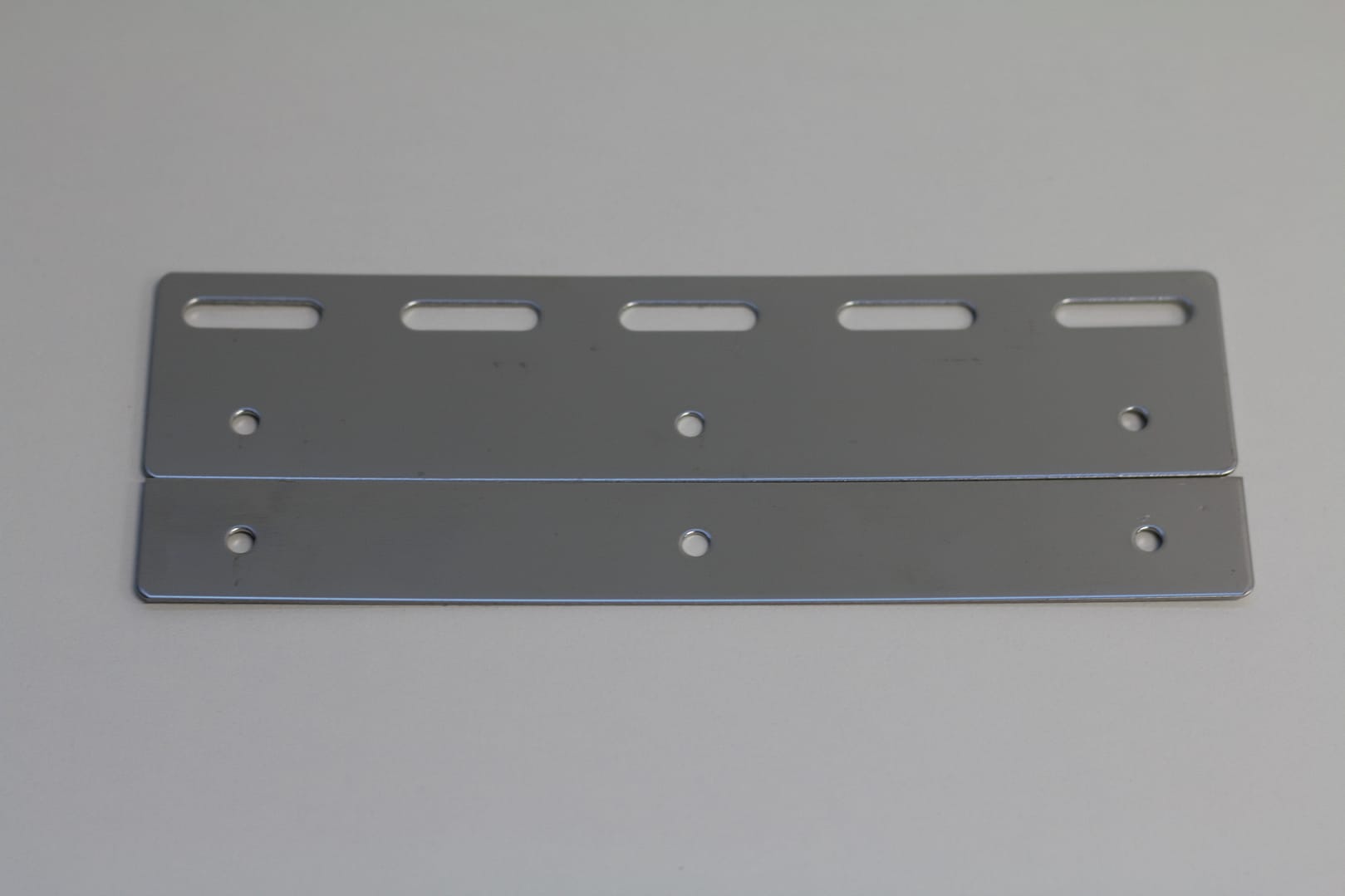 Two stainless steel mounting plates with pre-drilled holes and slots.