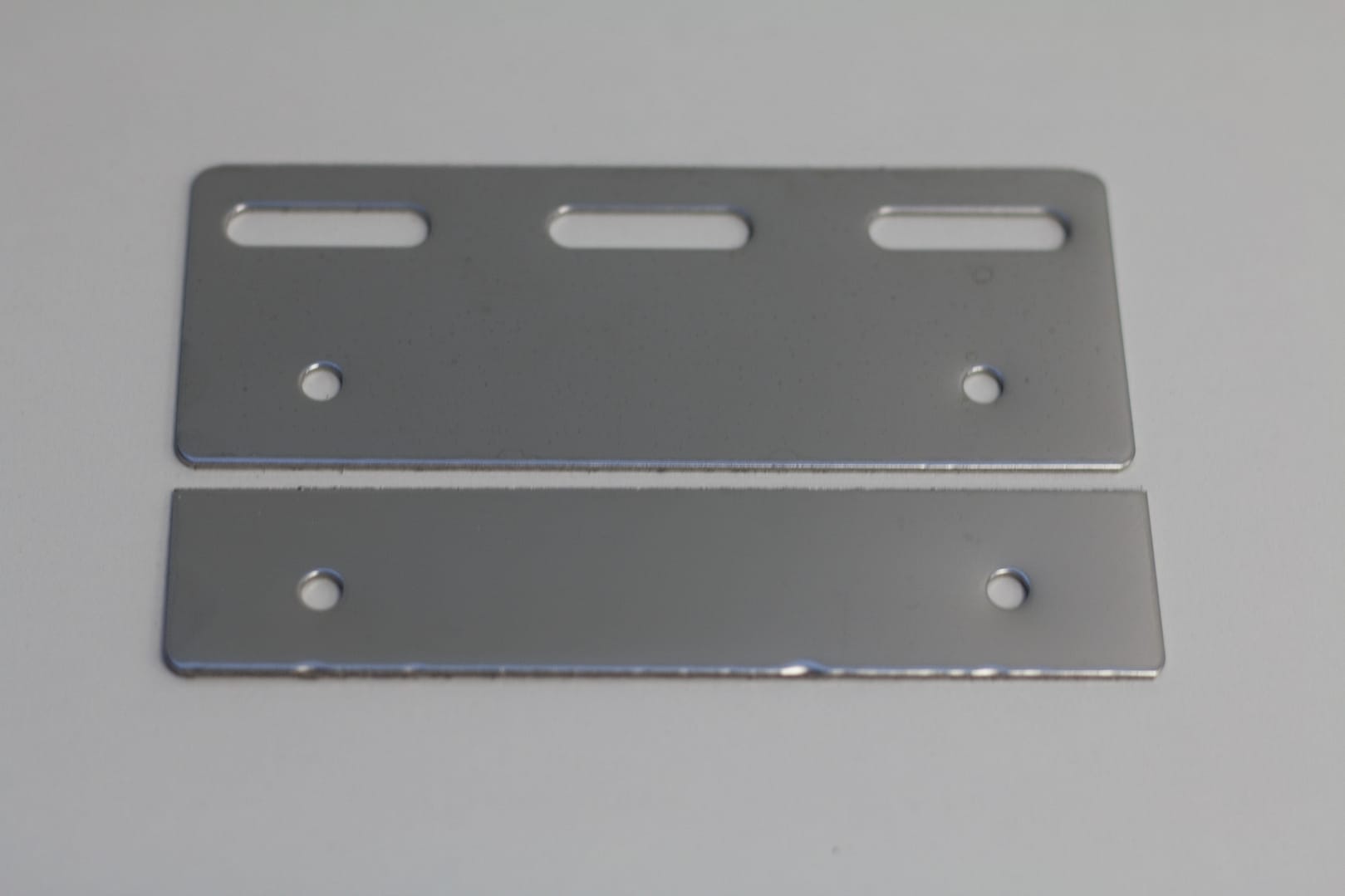 Two rectangular stainless steel mounting plates with pre-drilled holes and slots.