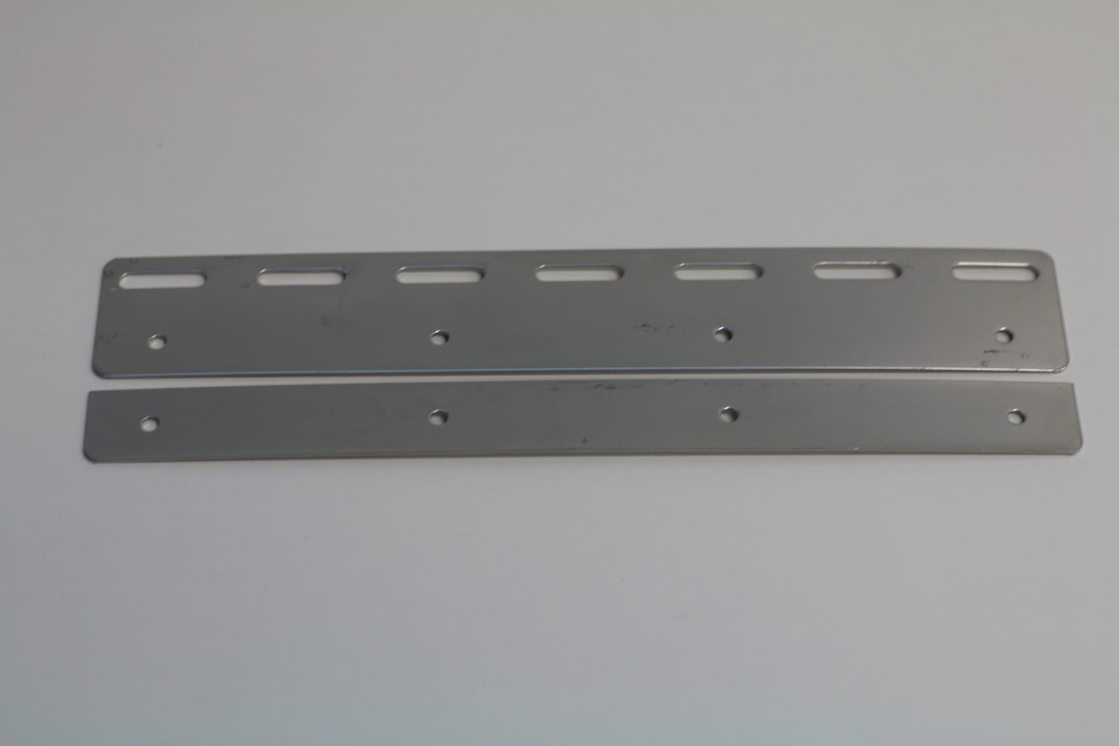 Two stainless steel mounting plates with pre-drilled holes and slots.