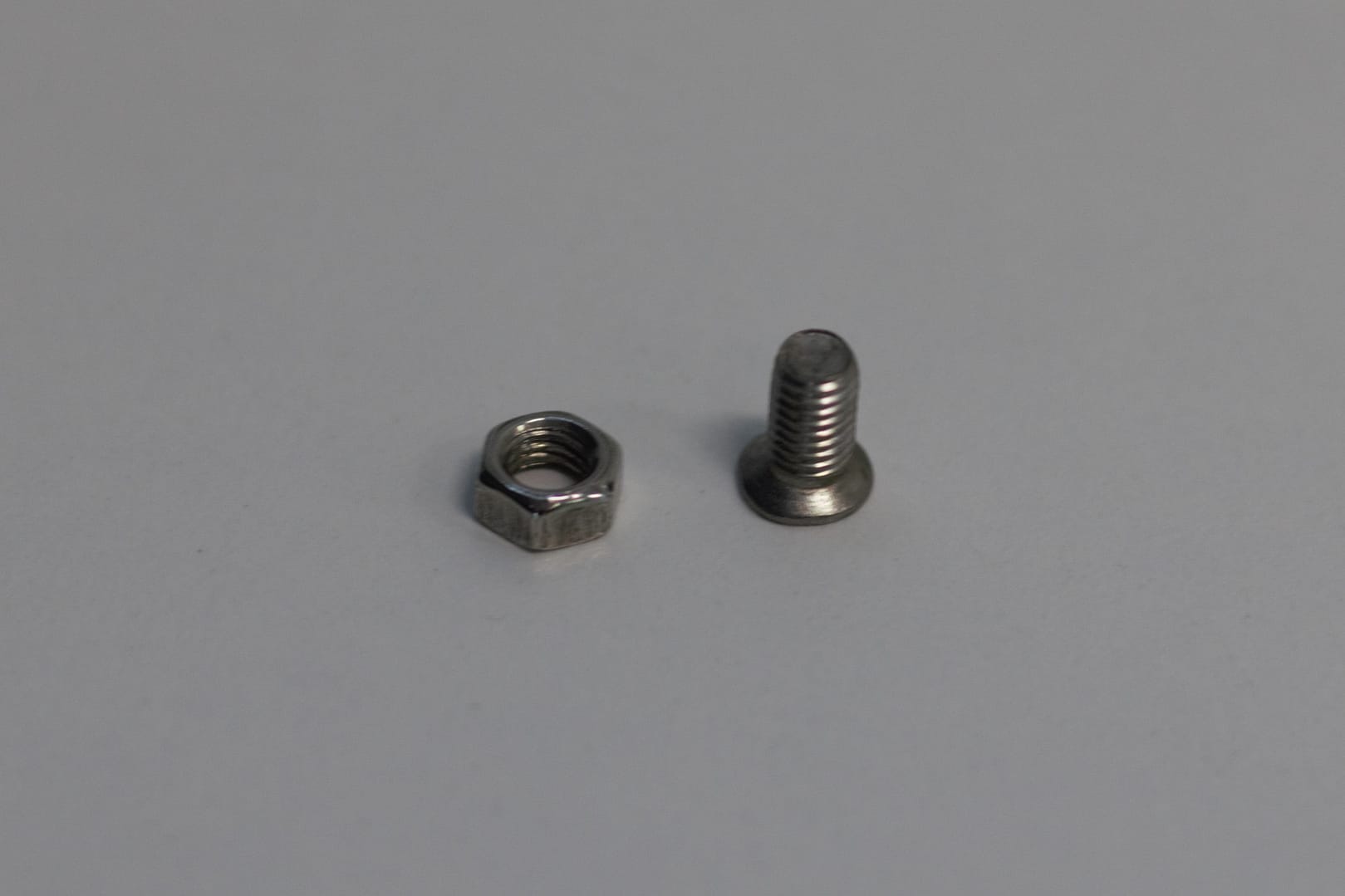 A small stainless steel hex nut and machine screw on a plain surface.
