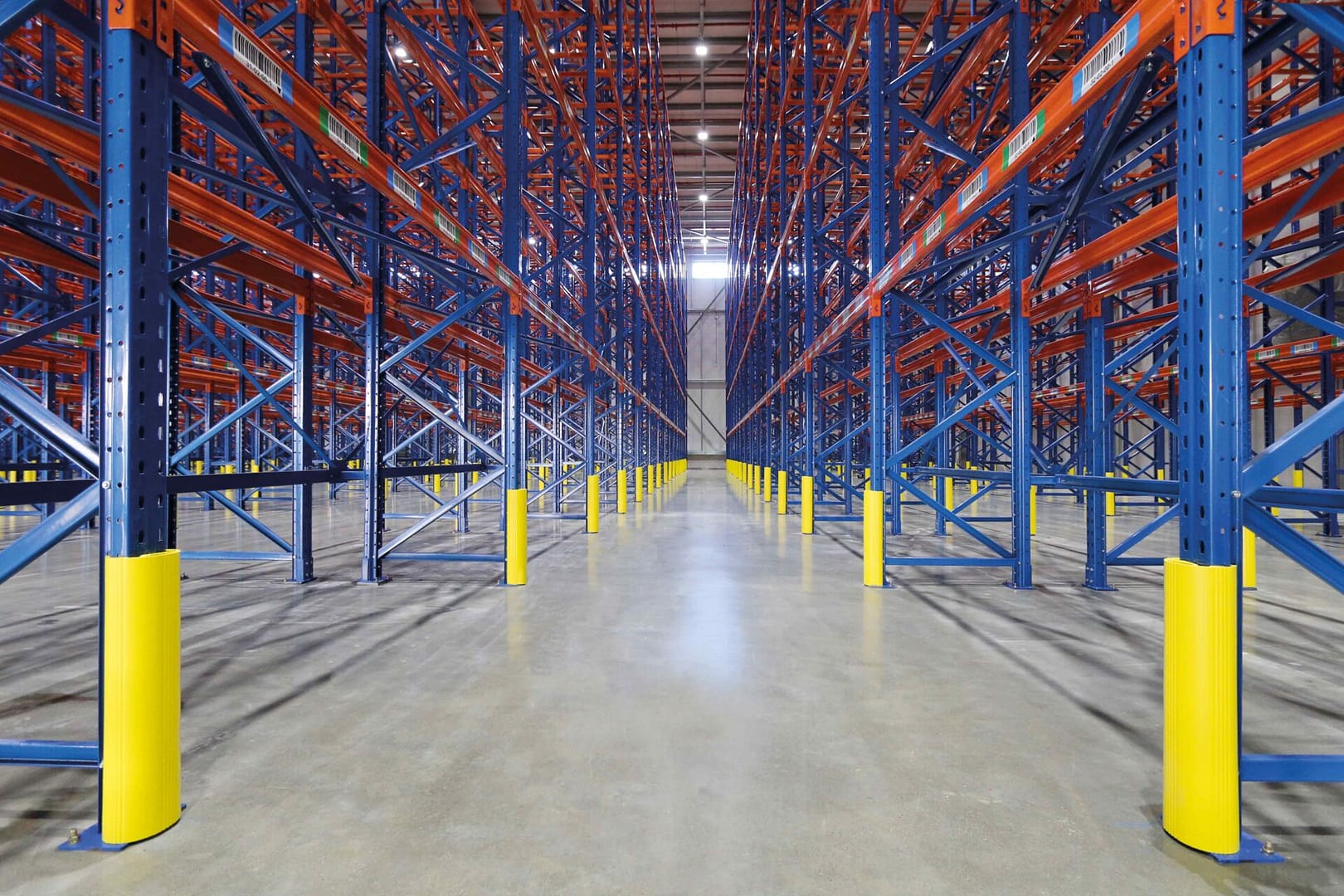 Yellow rack protectors installed on blue warehouse shelving uprights.