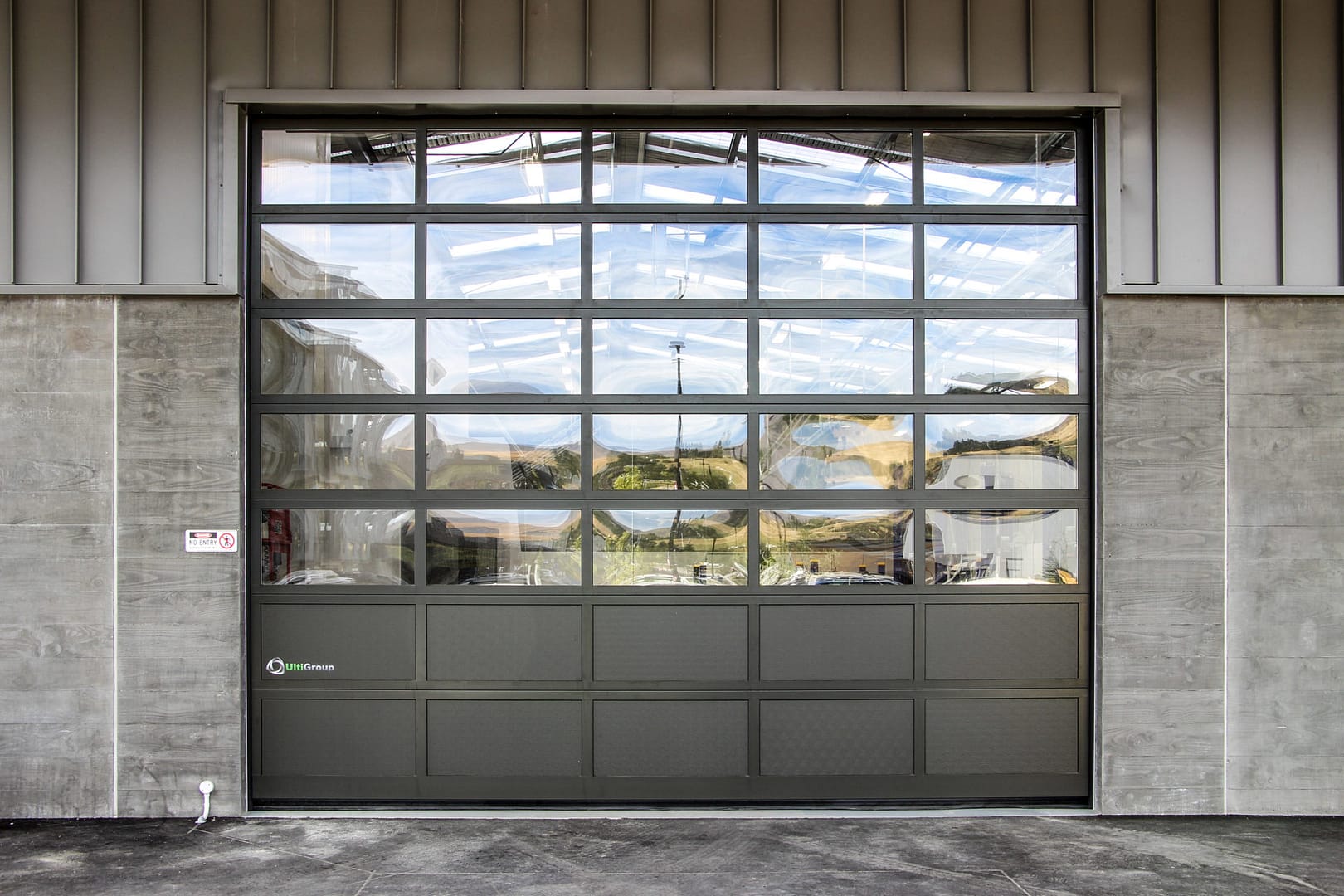 A glazed sectional industrial door with a dark grey frame and solid bottom panels.