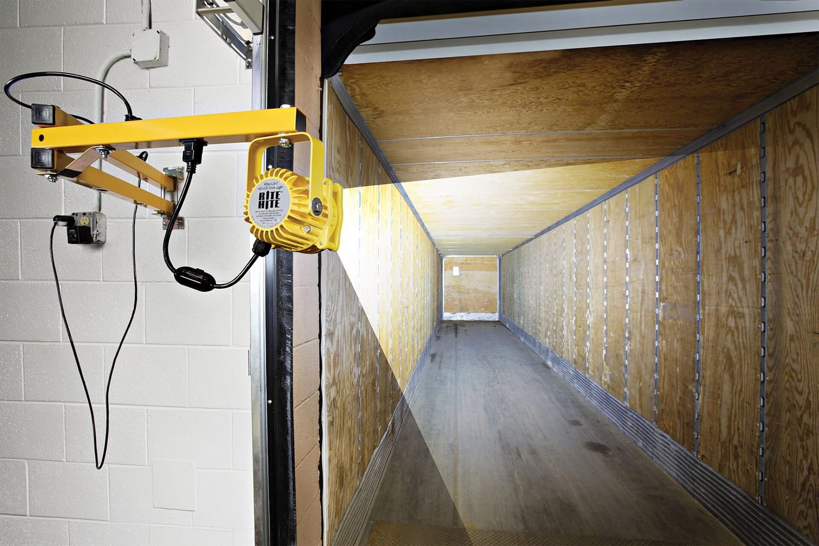 Yellow Rite-Lite LED dock light illuminating the interior of a shipping container.