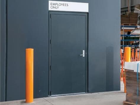 Grey industrial personnel door with Employees Only sign and orange bollard.