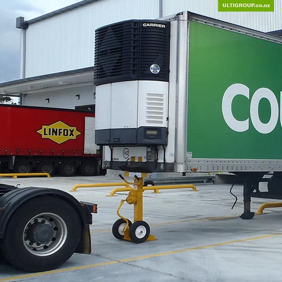Yellow trailer stand supporting a refrigerated semi-trailer at a loading dock.