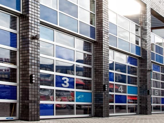 Sectional glass garage doors numbered three, four, and five on a tiled building.