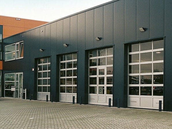 Four glazed sectional overhead doors installed on a dark grey industrial building.