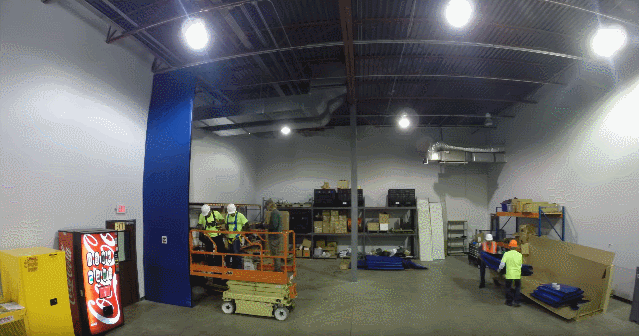 Technicians installing a blue industrial curtain wall using a scissor lift.