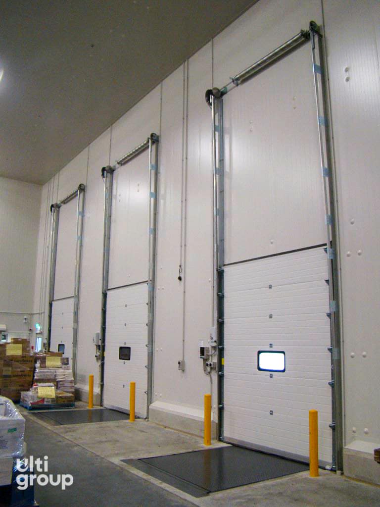 Three white sectional doors and dock levellers in a warehouse.