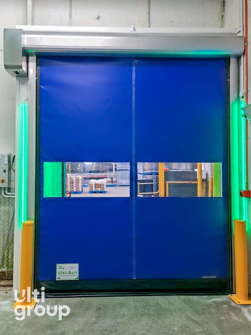 Blue Ulti-Roll high speed door with vision panels and green safety lights.