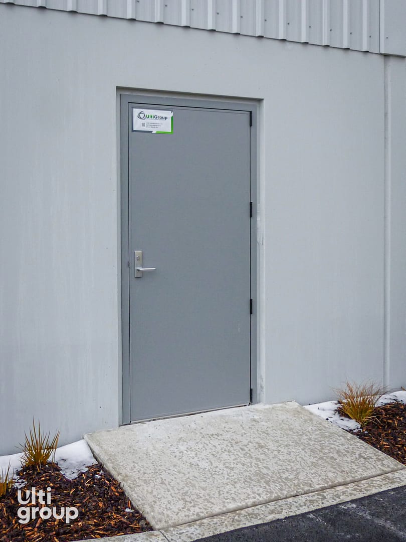 Grey steel personal access door installed in a concrete wall.