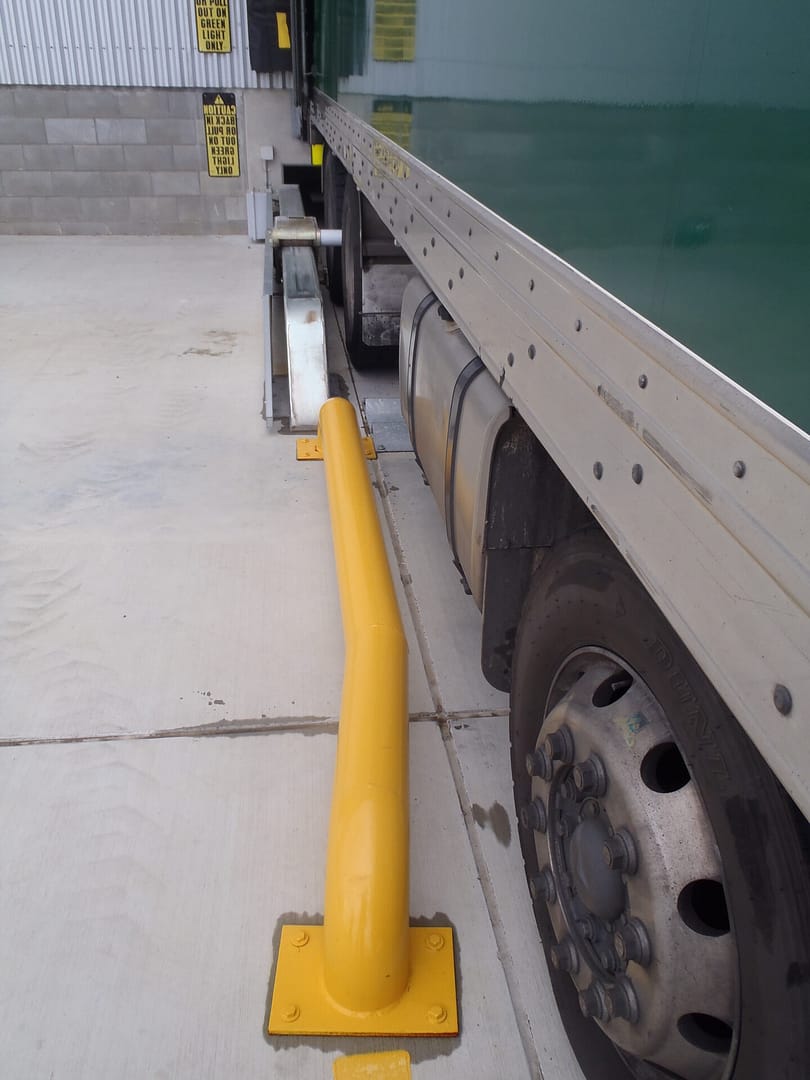 Yellow wheel guide and global wheel lock securing a truck at a loading dock.