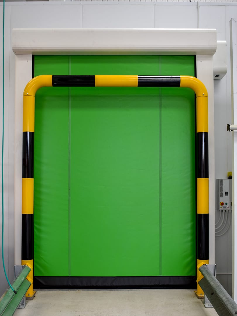 Green insulated high speed freezer door with yellow and black safety bollard.