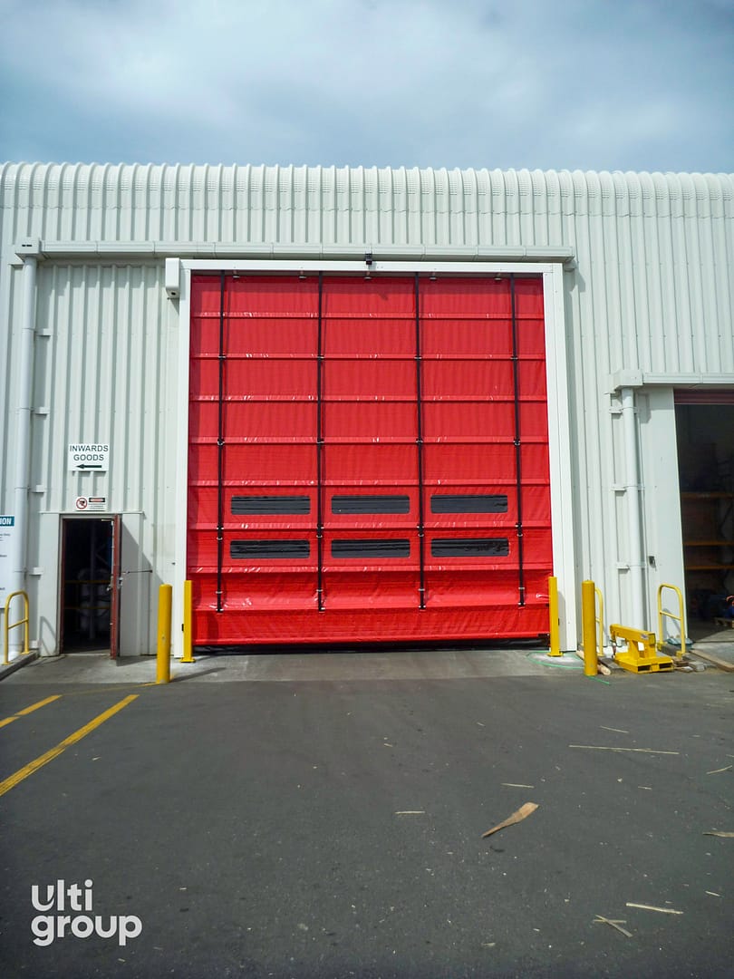 Red Ulti Fold Door installed on a corrugated metal warehouse exterior.