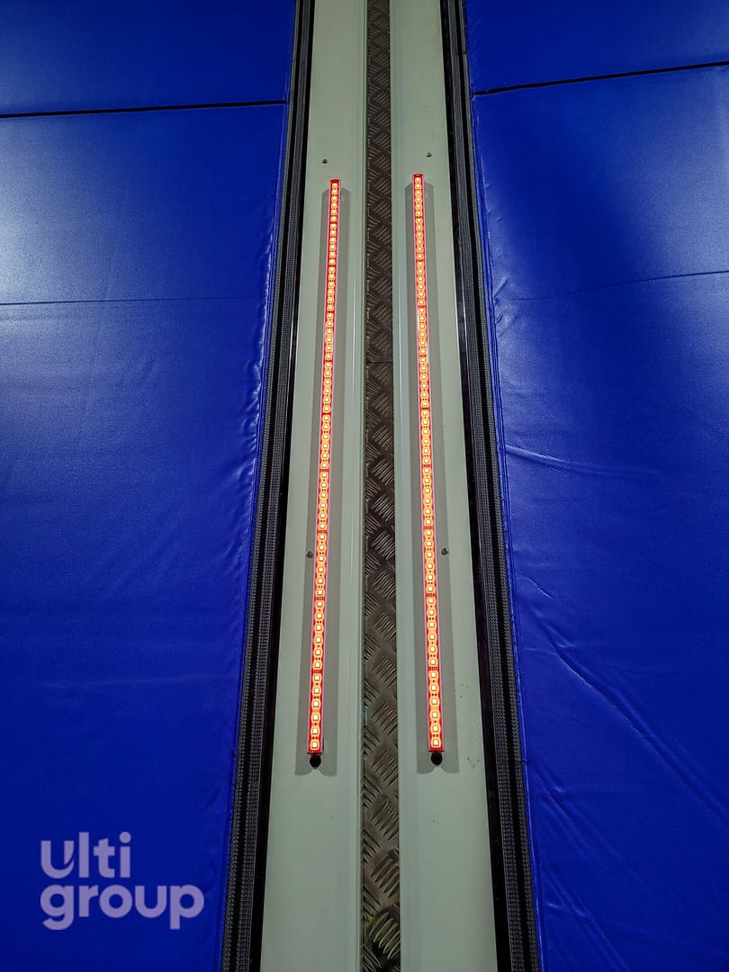 Red LED safety light strips on the side frames of a blue industrial door.
