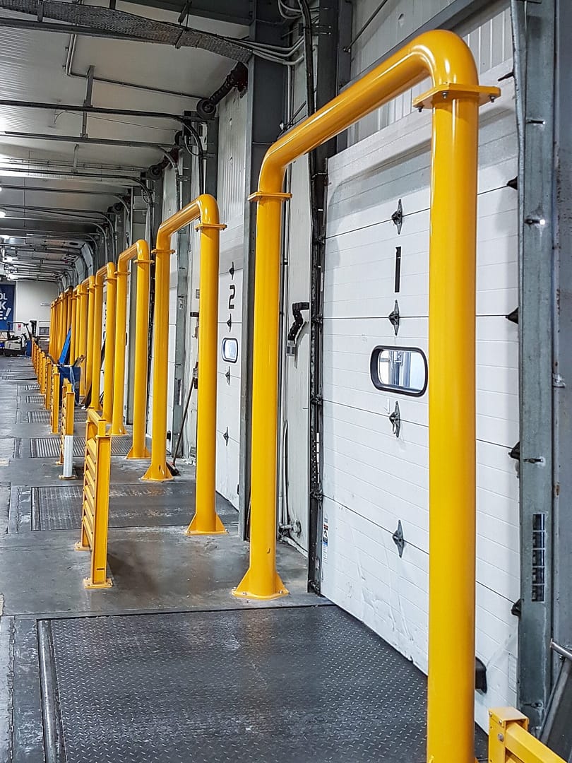 Yellow full frame bollards protecting white sectional dock doors in a warehouse.