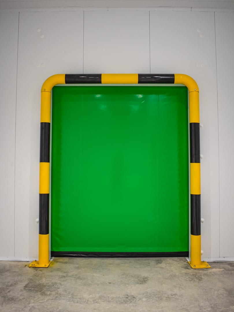 Green insulated high speed door with yellow and black safety bollard frame.