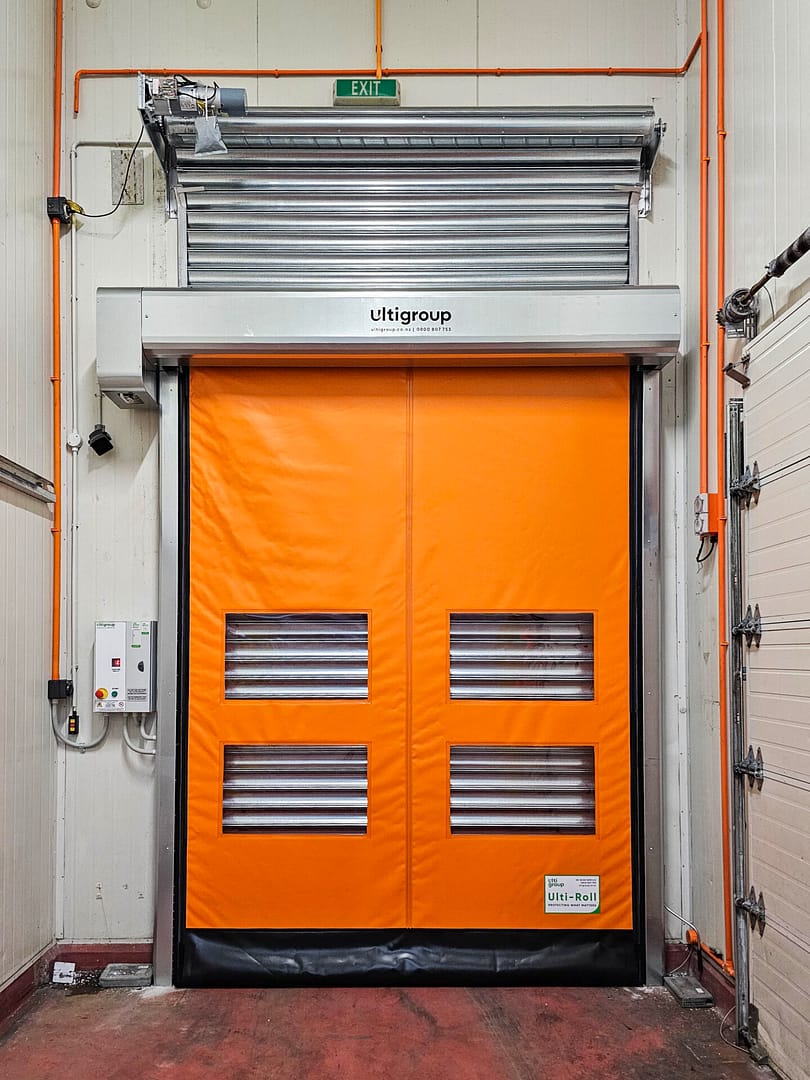 Orange Ulti Komby Door installed in a warehouse with a silver roller shutter above.