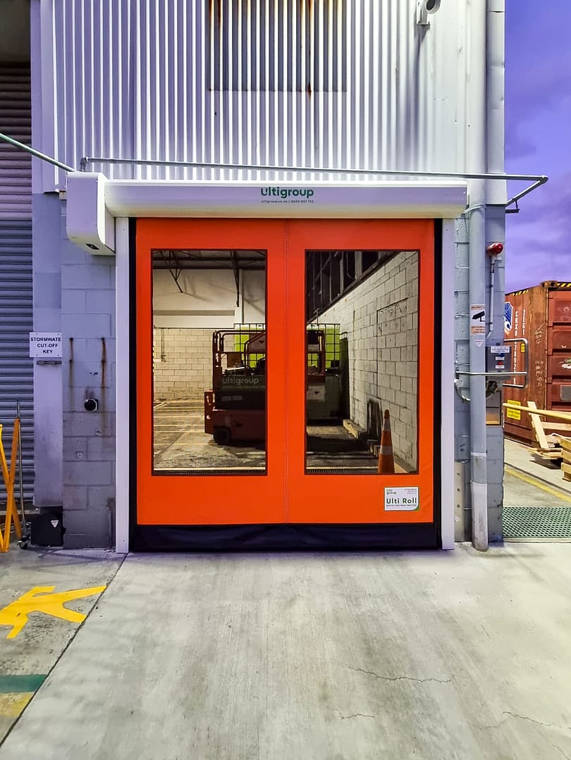 Orange Ulti Roll rapid door with large vision panels installed at a warehouse entrance.