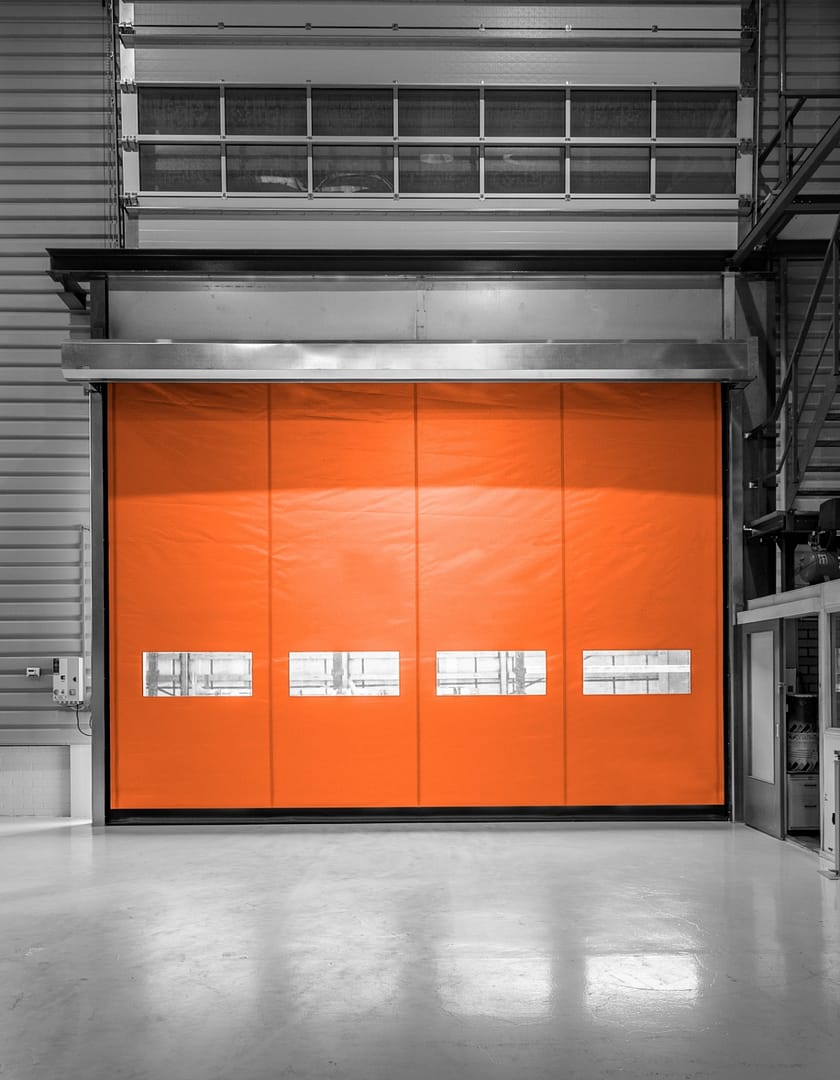 Orange Ulti Fold Door installed in a grey industrial warehouse facility.