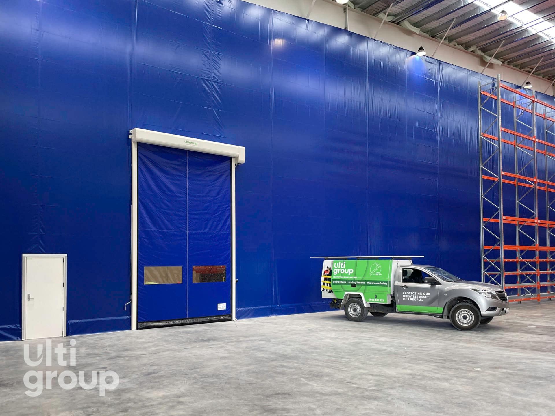 Ulti Roll door and PA door installed in a blue curtain wall partition.