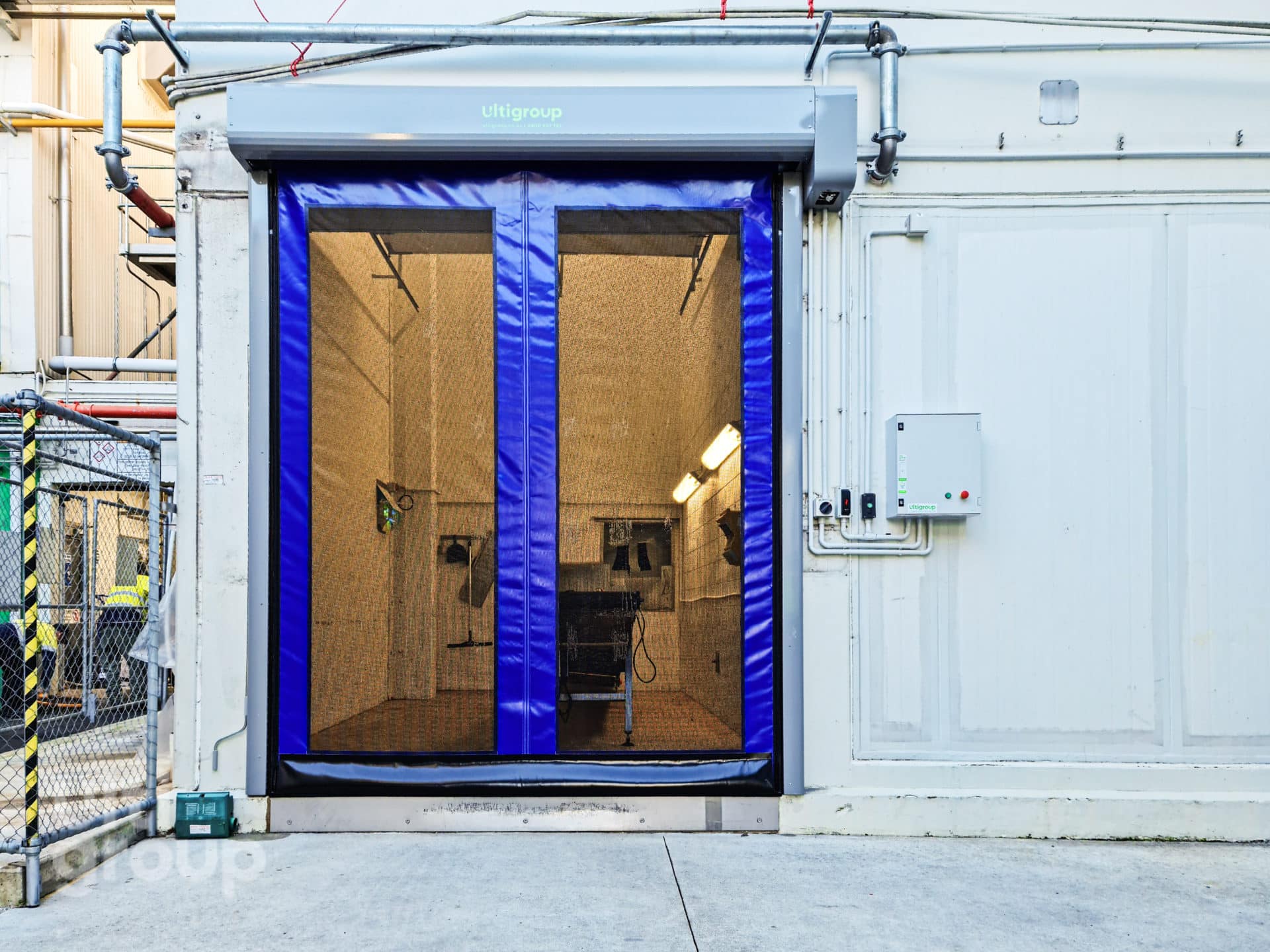 Blue industrial high speed door with mesh panels installed on a concrete wall.