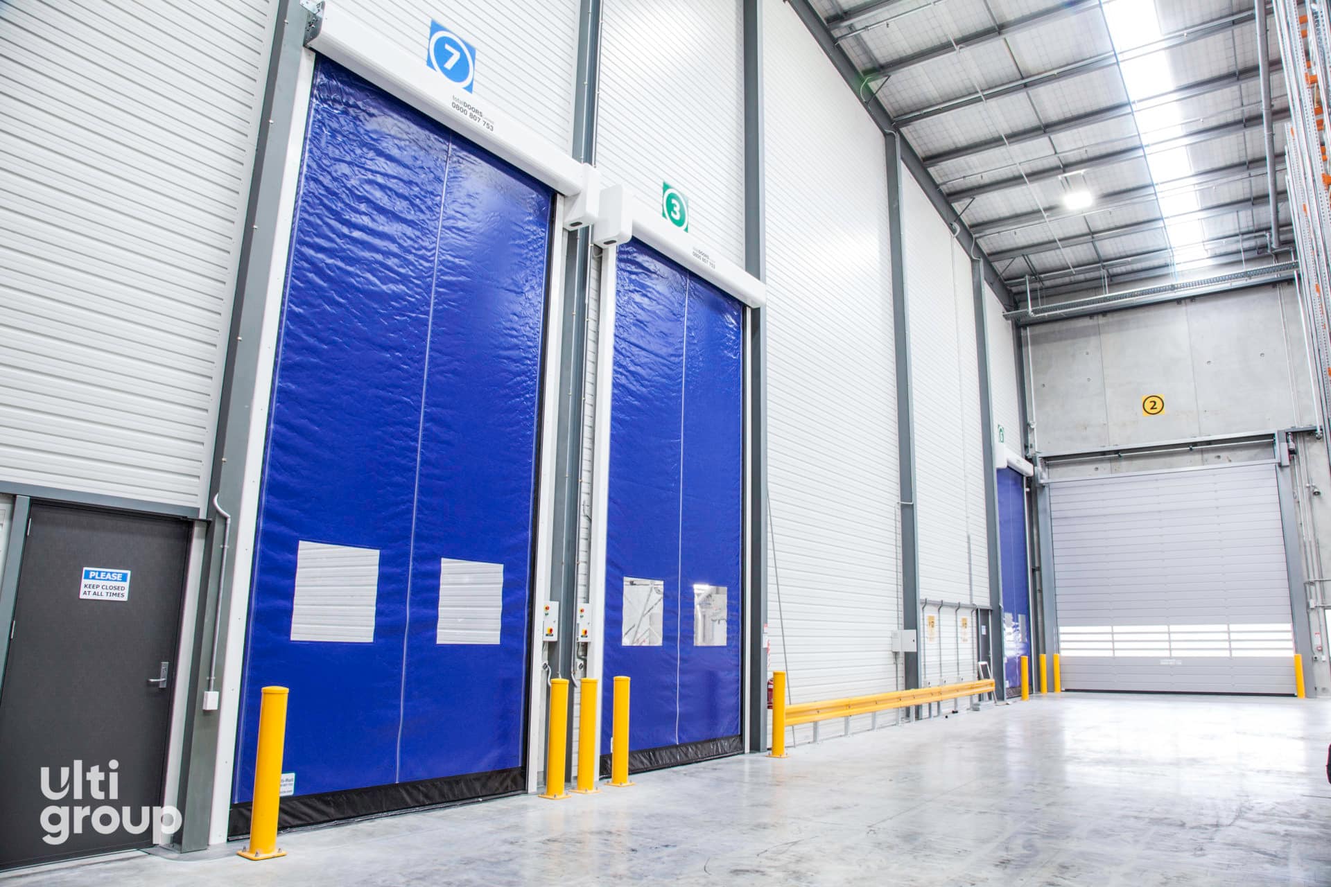 Blue rapid acting doors with vision panels and yellow safety bollards.