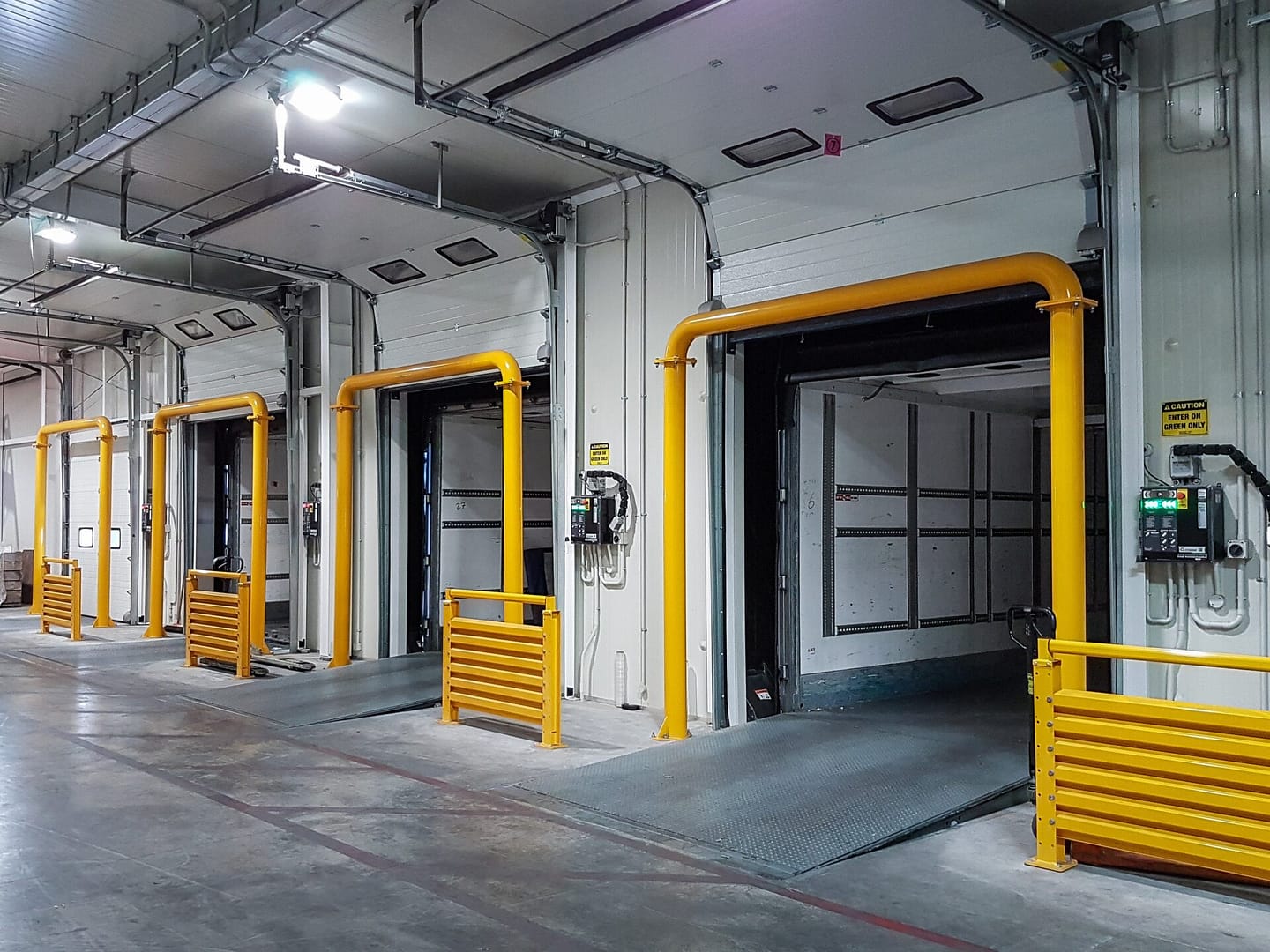 Yellow full frame bollards protecting loading dock doors in a warehouse.