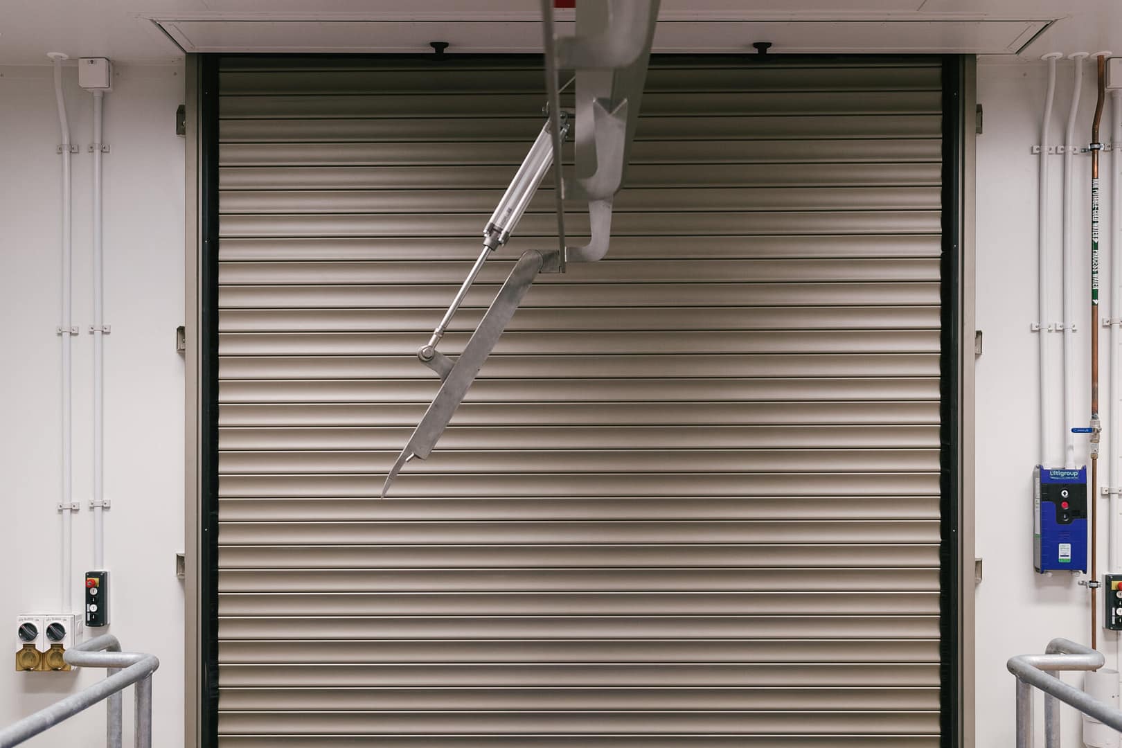 Industrial roller shutter door with overhead rail system and control panel.