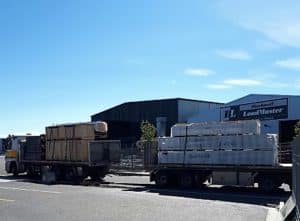 Truck and trailer unit loaded with construction materials outside a warehouse.