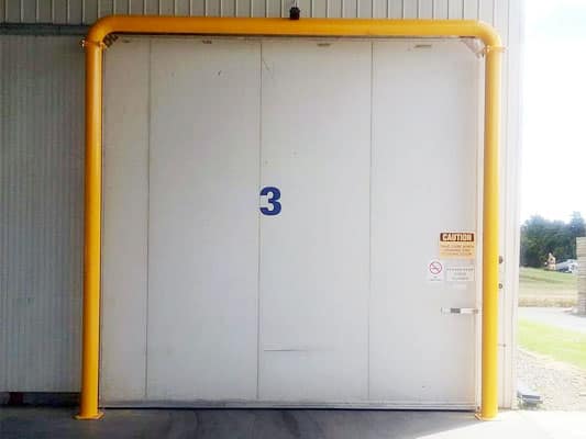 Large white industrial door with yellow protective bollard frame and number 3.